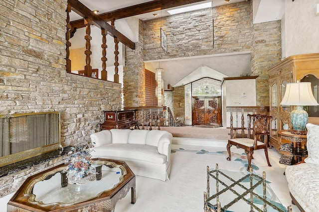 living room featuring beamed ceiling, a stone fireplace, and a high ceiling