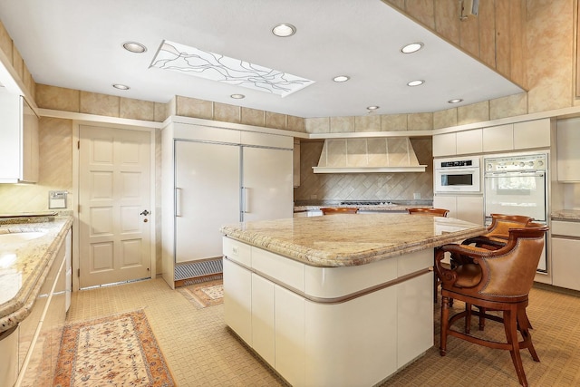 kitchen featuring custom exhaust hood, tasteful backsplash, a center island, and paneled built in fridge