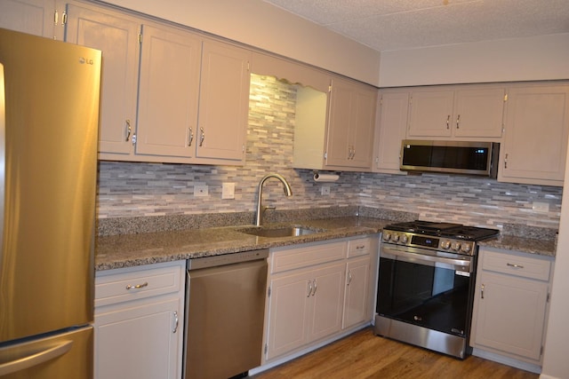 kitchen featuring sink, tasteful backsplash, light hardwood / wood-style flooring, stainless steel appliances, and light stone countertops