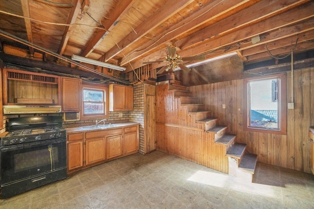 kitchen with black gas range, sink, ceiling fan, and wood walls