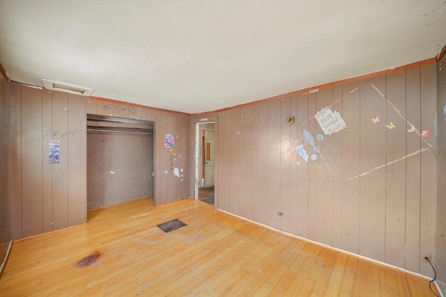 unfurnished bedroom with hardwood / wood-style flooring, wooden walls, and a closet