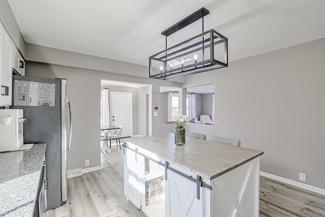 kitchen featuring stainless steel refrigerator, white cabinetry, hanging light fixtures, light hardwood / wood-style floors, and light stone countertops