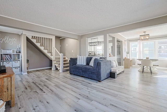 living room with an inviting chandelier, crown molding, a textured ceiling, and light wood-type flooring