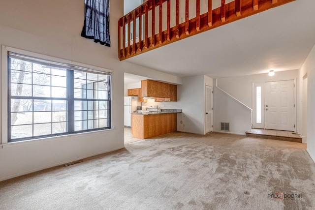 unfurnished living room featuring light carpet and a high ceiling