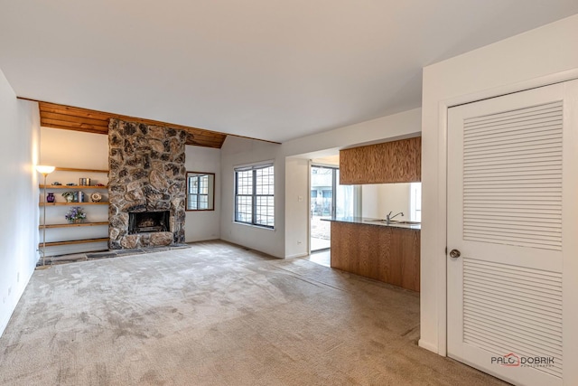 unfurnished living room with lofted ceiling, a stone fireplace, sink, and light carpet