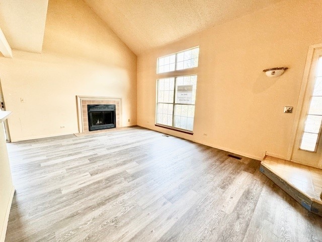 unfurnished living room with a tiled fireplace, light hardwood / wood-style flooring, high vaulted ceiling, and a textured ceiling