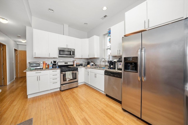 kitchen with light wood-type flooring, white cabinetry, stainless steel appliances, and a sink