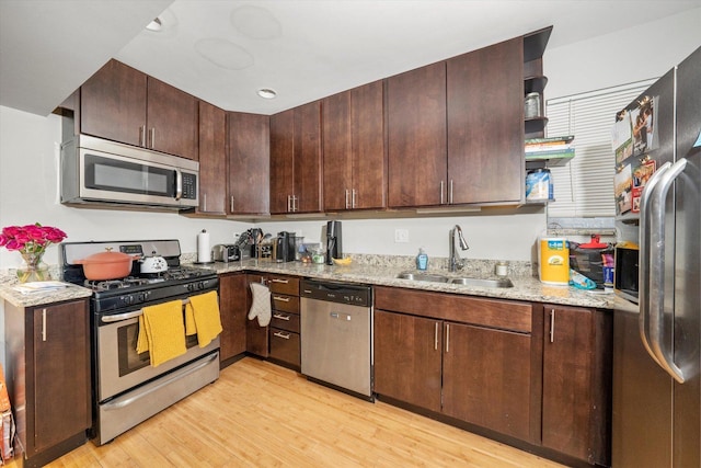 kitchen featuring a sink, dark brown cabinets, appliances with stainless steel finishes, light stone countertops, and light wood finished floors