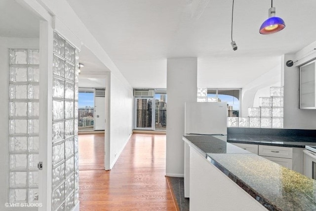 kitchen with hardwood / wood-style floors, hanging light fixtures, white cabinets, dark stone counters, and white fridge