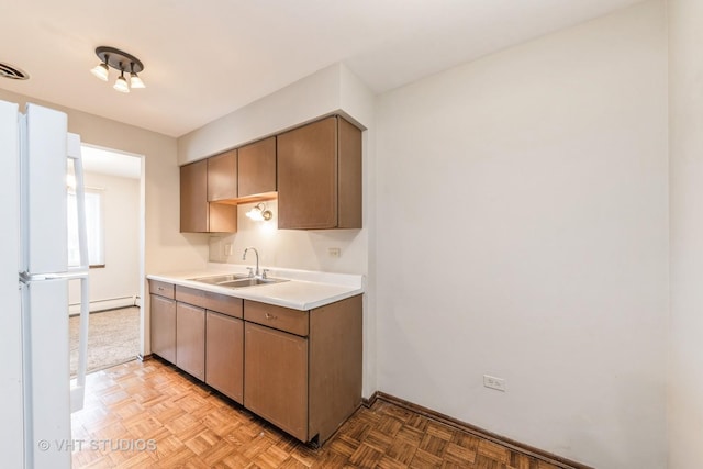 kitchen with light countertops, baseboard heating, a sink, and freestanding refrigerator