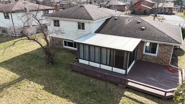 rear view of property featuring a lawn, a sunroom, and a deck