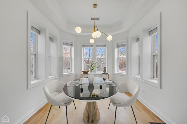 dining room featuring wood finished floors, visible vents, baseboards, ornamental molding, and a tray ceiling