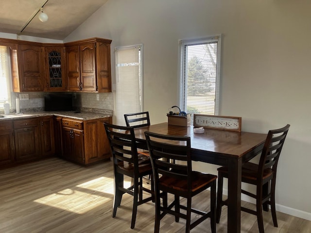 dining space with track lighting, lofted ceiling, and light wood-type flooring