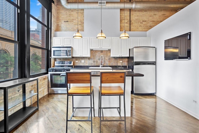 kitchen with sink, appliances with stainless steel finishes, white cabinetry, a towering ceiling, and decorative backsplash