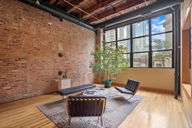 sitting room featuring hardwood / wood-style flooring, a towering ceiling, and brick wall