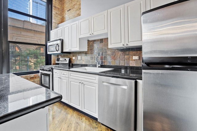 kitchen with stainless steel appliances, white cabinetry, sink, and dark stone counters