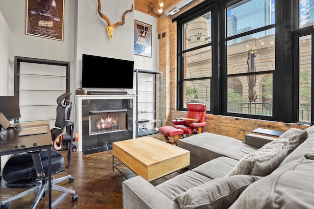 living room featuring a tile fireplace, dark hardwood / wood-style floors, brick wall, and a high ceiling