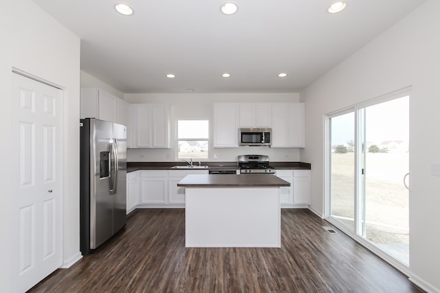 kitchen with dark wood-type flooring, sink, white cabinetry, a kitchen island, and stainless steel appliances