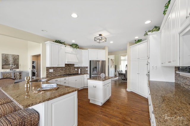 kitchen with sink, a center island, dark stone counters, and stainless steel refrigerator with ice dispenser