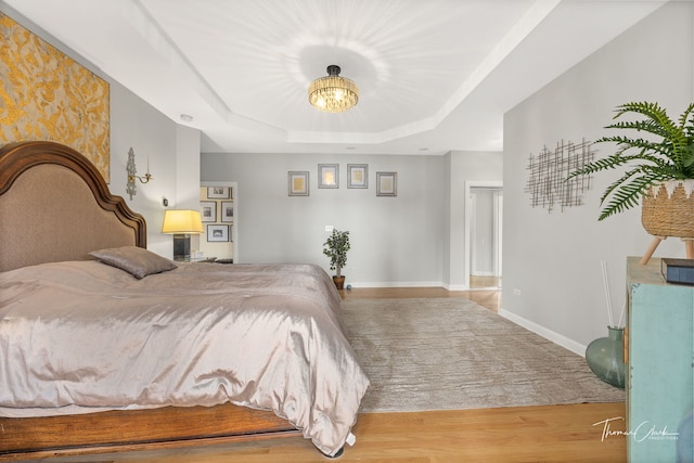 bedroom featuring light hardwood / wood-style flooring, a chandelier, and a tray ceiling