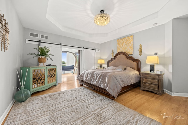 bedroom featuring access to exterior, a chandelier, a tray ceiling, hardwood / wood-style flooring, and a barn door