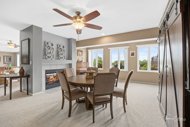 carpeted dining space featuring a fireplace, plenty of natural light, a barn door, and ceiling fan