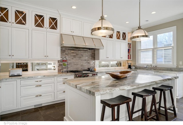 kitchen with white cabinetry, hanging light fixtures, ornamental molding, a kitchen breakfast bar, and a kitchen island