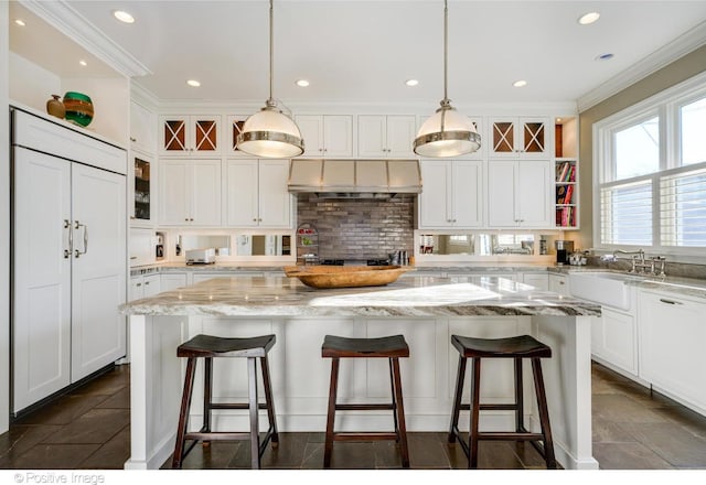 kitchen with decorative light fixtures, a center island, light stone countertops, and exhaust hood