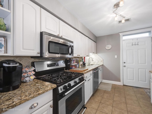 kitchen with sink, dark stone countertops, white cabinets, stainless steel appliances, and backsplash