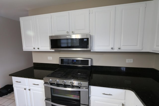 kitchen with light tile patterned flooring, dark stone counters, white cabinets, and appliances with stainless steel finishes