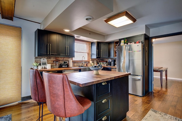 kitchen featuring a kitchen island, butcher block counters, stainless steel fridge, a kitchen bar, and light wood-type flooring