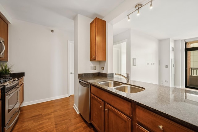 kitchen with appliances with stainless steel finishes, sink, dark hardwood / wood-style flooring, and dark stone counters