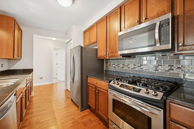 kitchen with decorative backsplash, stainless steel appliances, light hardwood / wood-style floors, and dark stone counters