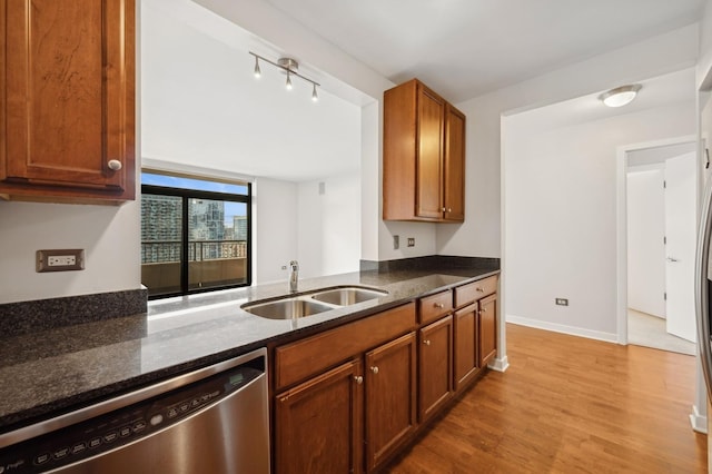 kitchen featuring sink, stainless steel dishwasher, light wood-type flooring, and dark stone counters