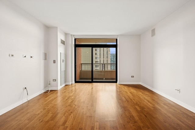 spare room with a wall of windows and light hardwood / wood-style floors