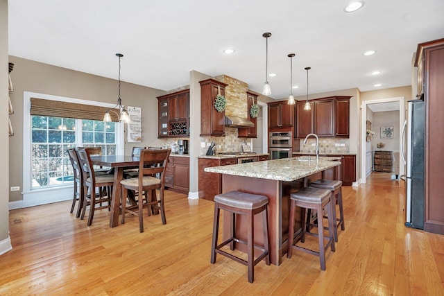 kitchen with a breakfast bar, tasteful backsplash, decorative light fixtures, a center island with sink, and stainless steel appliances