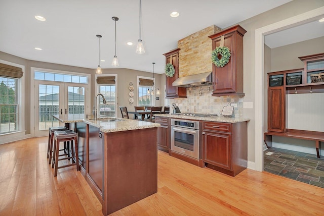 kitchen featuring sink, hanging light fixtures, light stone counters, extractor fan, and oven