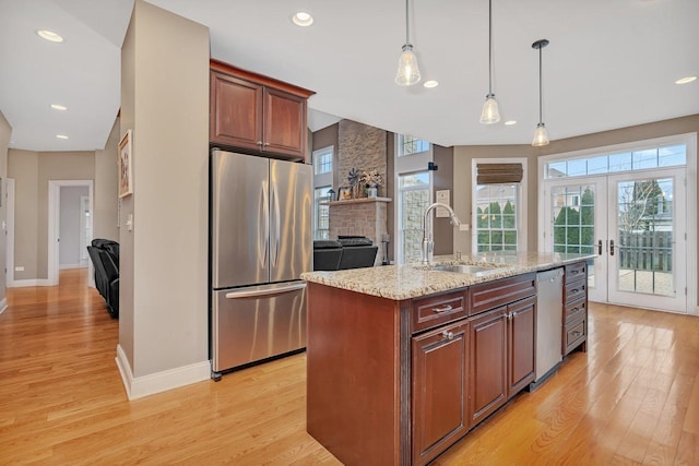 kitchen with sink, a center island with sink, light stone countertops, and appliances with stainless steel finishes