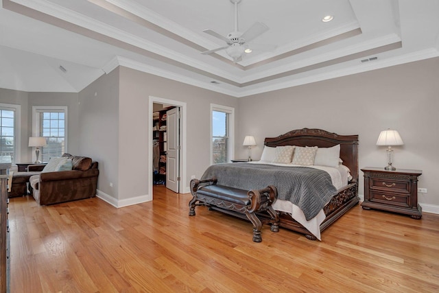 bedroom featuring a walk in closet, light wood-type flooring, ornamental molding, a tray ceiling, and ceiling fan