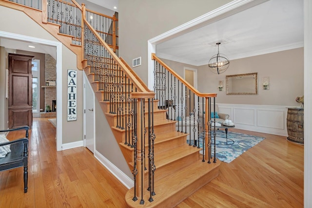 stairs featuring crown molding, wood-type flooring, a chandelier, a large fireplace, and a towering ceiling