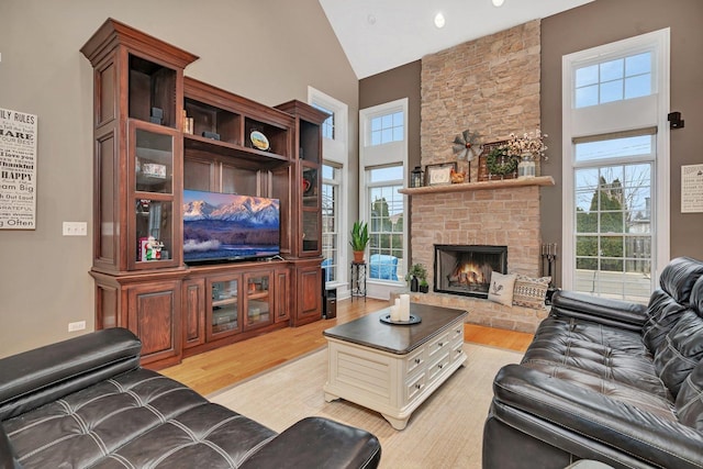 living room featuring a stone fireplace, high vaulted ceiling, and light hardwood / wood-style flooring