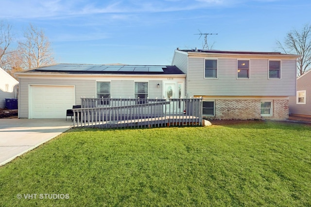 split level home with a front yard, concrete driveway, an attached garage, roof mounted solar panels, and brick siding