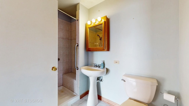 bathroom featuring tile patterned flooring, baseboards, a tile shower, and toilet