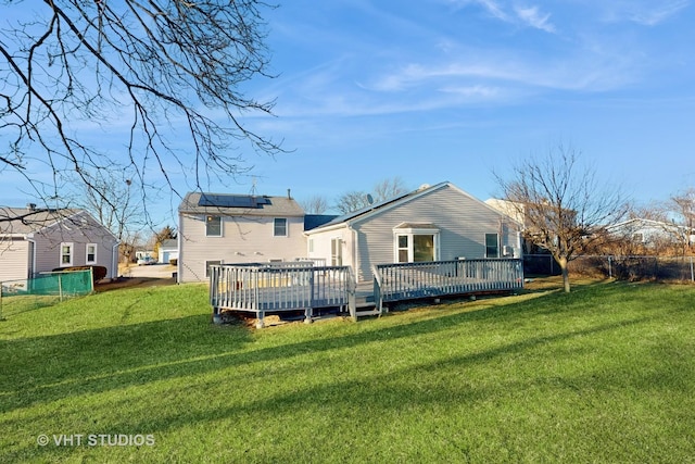 rear view of house featuring roof mounted solar panels, a lawn, a deck, and fence