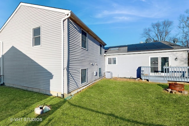 rear view of property featuring a deck, a lawn, and roof mounted solar panels