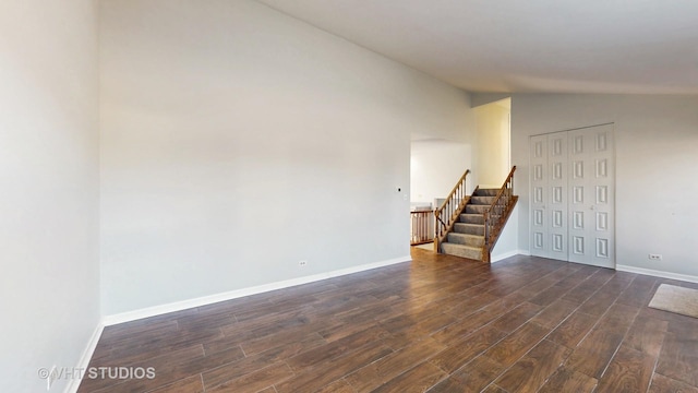 empty room featuring dark wood-style floors, lofted ceiling, stairway, and baseboards