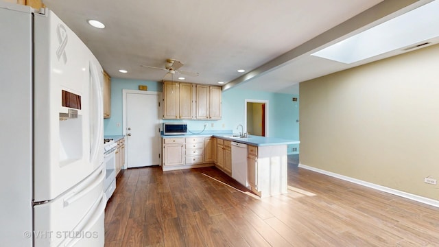 kitchen featuring a peninsula, white appliances, a skylight, a sink, and light brown cabinetry