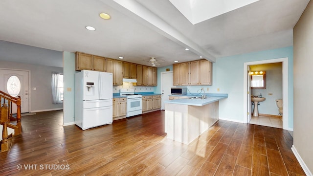 kitchen featuring white appliances, dark wood finished floors, under cabinet range hood, and a peninsula