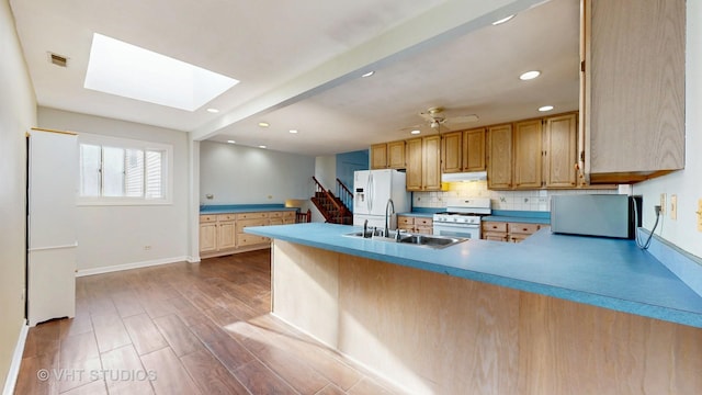 kitchen featuring under cabinet range hood, a peninsula, white appliances, a sink, and decorative backsplash