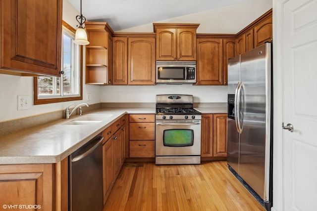 kitchen with appliances with stainless steel finishes, pendant lighting, lofted ceiling, sink, and light hardwood / wood-style flooring